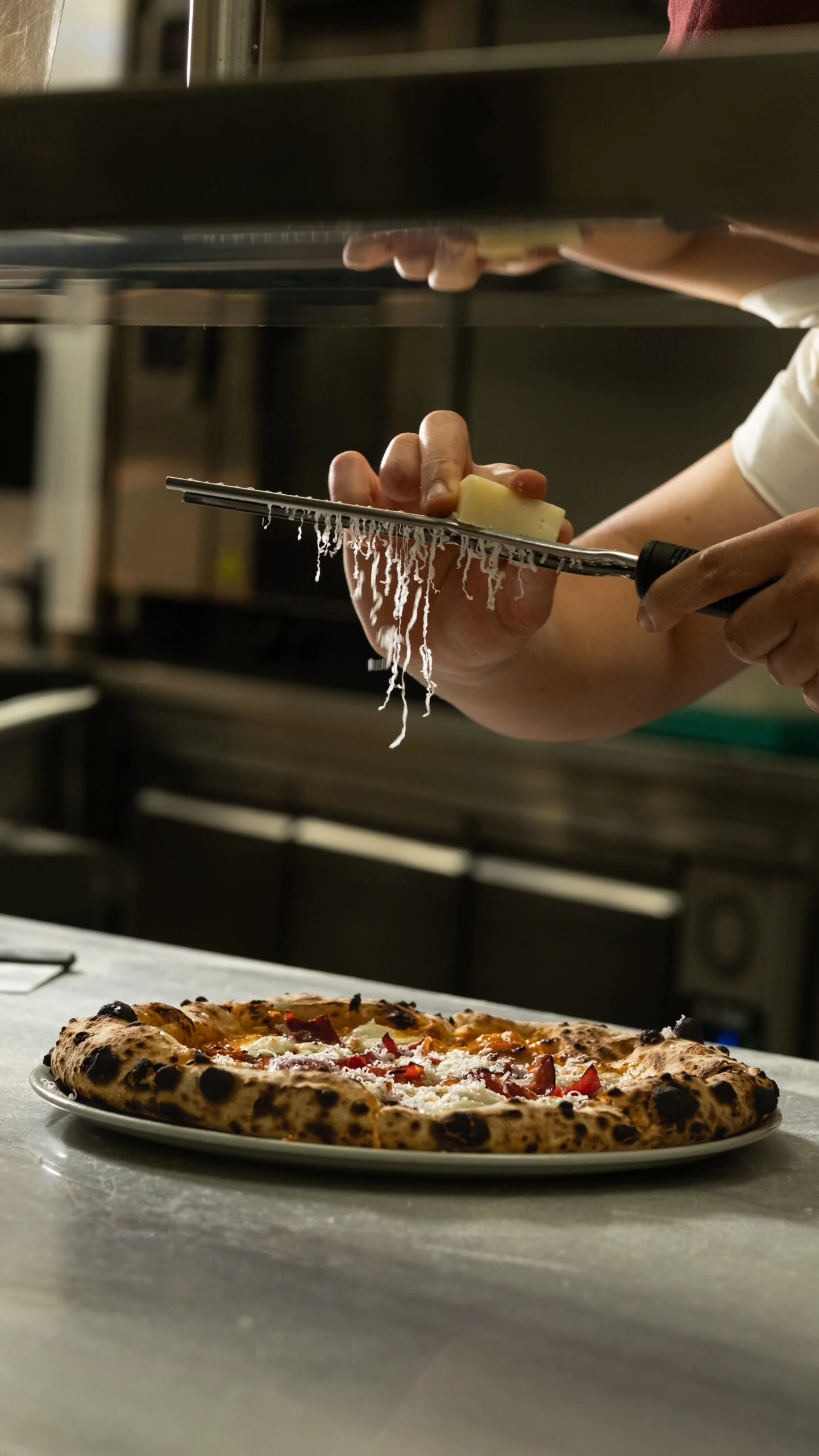 Handwork in the kitchen: the chef grating fresh cheese over a pizza from the oven